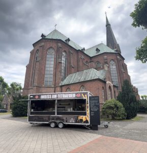 Foodtruck mit geöffneter Ausgabe vor einer Backsteinkirche
