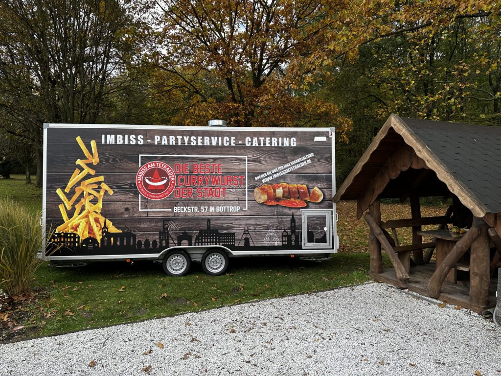 Foodtruck des Imbiss am Tetraeder auf einer Grünfläche neben einer Holzhütte